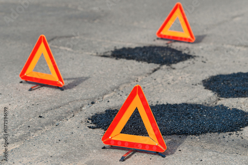 Fresh asphalt patches marked by warning triangles for safety. Asphalt patchwork. Road repair. Asphalt patch on damaged road.