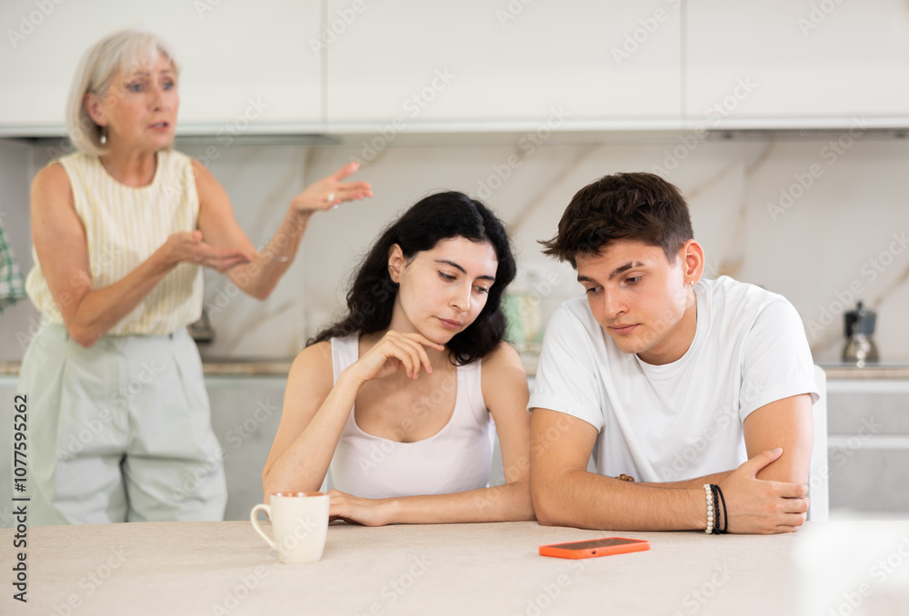 Elderly mom make claims to young couple in home kitchen Elderly mom make claims to young couple in home kitchen
