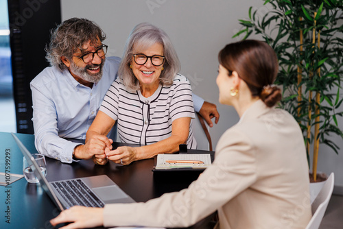 Happy senior couple holding hands while listening to financial advisor photo