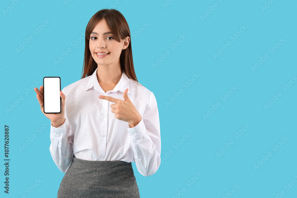 Beautiful young businesswoman pointing at mobile phone on blue background