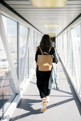 Woman walks down a brightly lit airport jet bridge. photo