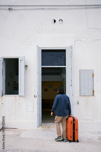 Man with orange suitcase outside a white house photo