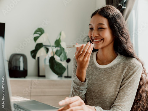 Smiling Woman Engages in Virtual Meeting Using Smartphone and Laptop photo