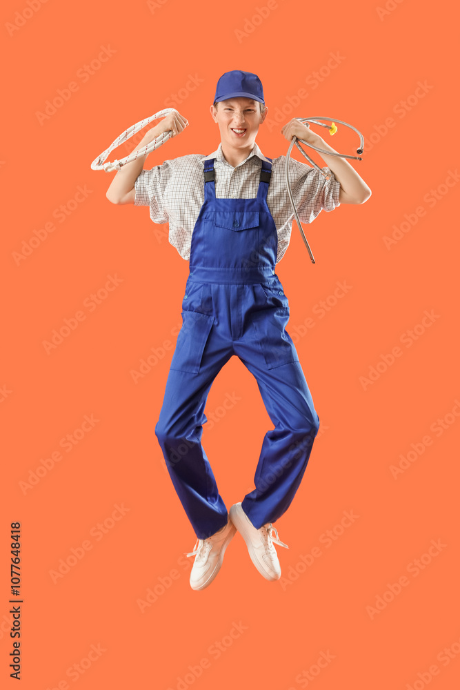 Jumping male plumber with hoses on orange background Jumping male plumber with hoses on orange background