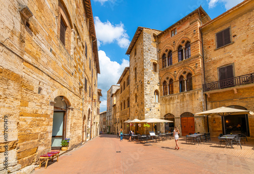 Fototapeta Naklejka Na Ścianę i Meble -  Sidewalk cafes and shops in the historic medieval center of the Italian hill town of San Gimignano, Italy, in the Siena Province of the region of Tuscany.