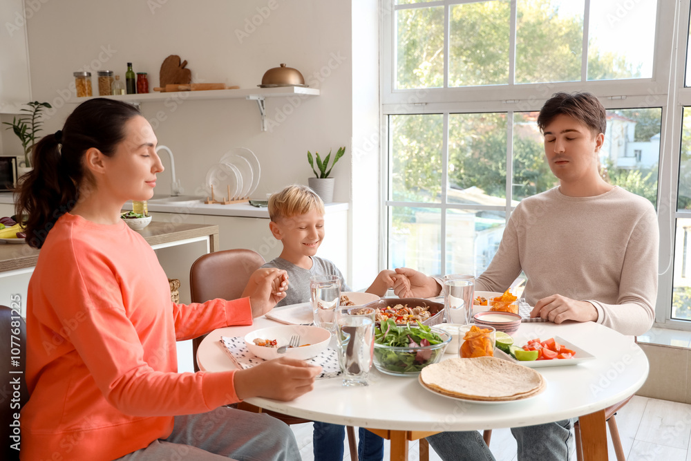 Little boy with his parents praying before eating Fajita at table in kitchen Little boy with his parents praying before eating Fajita at table in kitchen