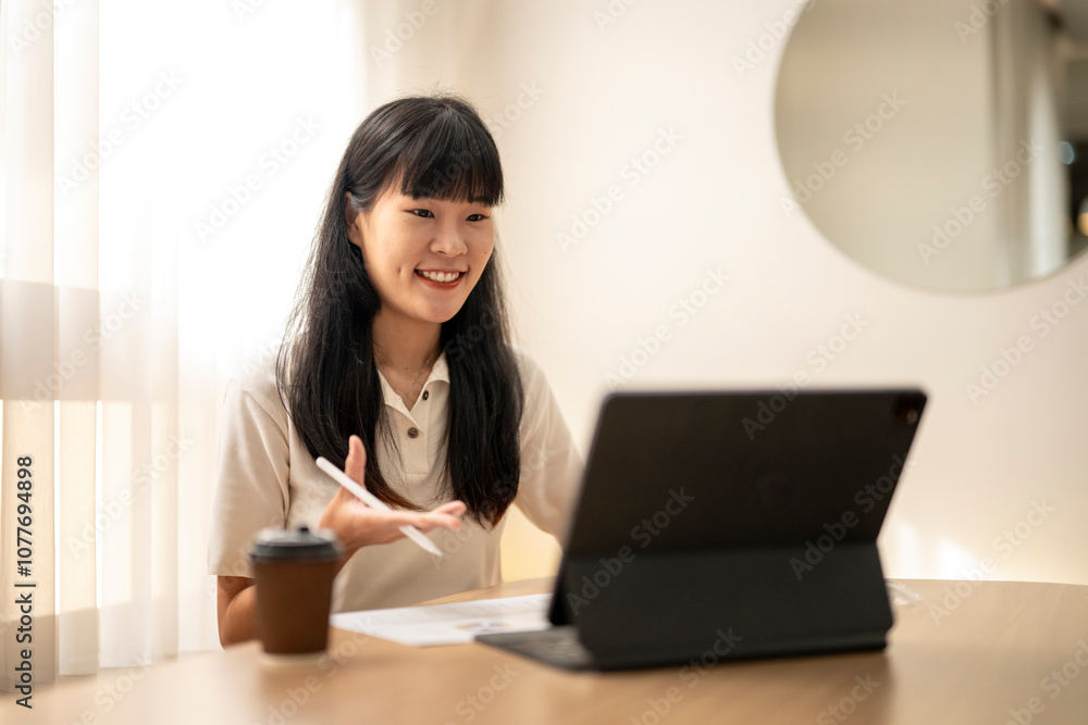 Young asian woman having video call on tablet and taking notes at home office Young asian woman having video call on tablet and taking notes at home office
