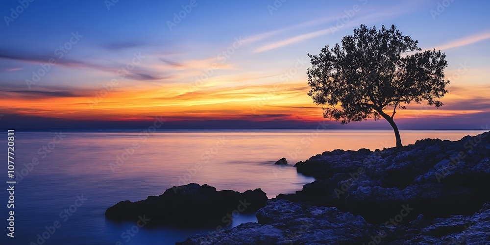 Solitary Tree Silhouetted Against a Vibrant Sunset Over the Sea Solitary Tree Silhouetted Against a Vibrant Sunset Over the Sea