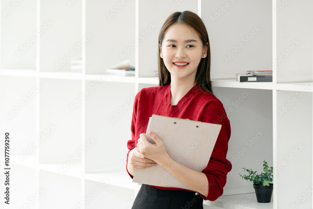 Happy asain woman in red sweater holding clipboard standing in modern office. Happy asain woman in red sweater holding clipboard standing in modern office.