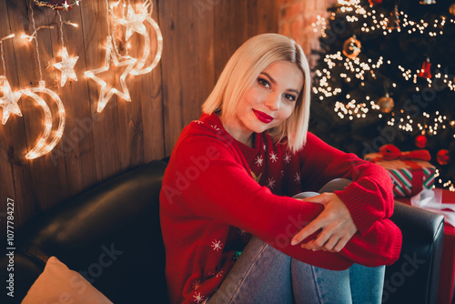 Photo of nice young blonde girl hugging knees cozy wear christmas sweater enjoy cozy x-mas party decoration interior flat indoors photo