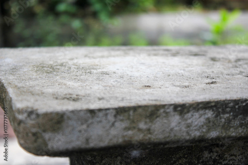 A weathered stone table stands alone in a garden, its surface worn and textured