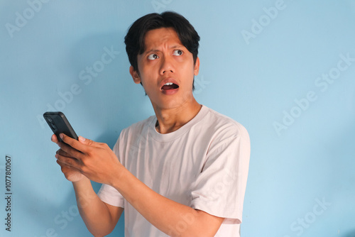 Young asian man showing confused expression while holding mobile phone  photo