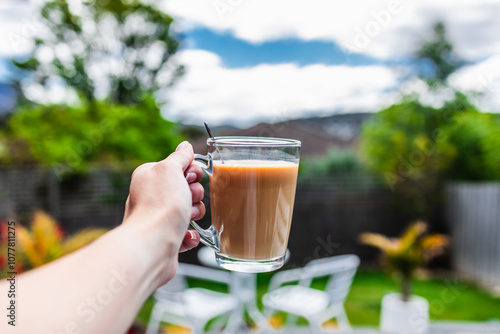 Foto hand holding coffee in clear mug in front of blurred home interior background, h
