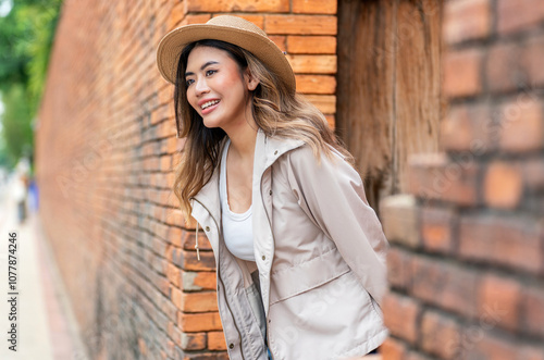 Asian Tourist Woman In Hat and Jacket Using Phone Beside A Brick Wall in Chiang Mai, Thailand photo