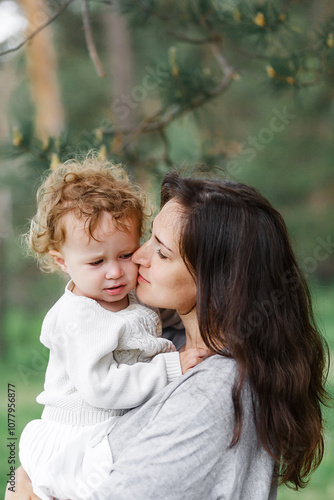 young mother holding her daughter and walking in green forest on a summer sunny day. Family having fun together. Childhood, parenting, happiness concept. mother's day. 