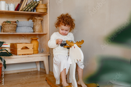 Portrait of funny young retro girl photographer in white clothes at home background, holds camera in hands, looks into camera serious