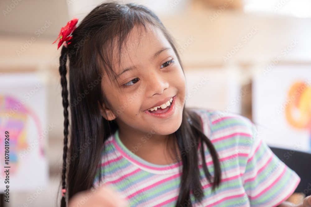 Asian joyful young girl with Down syndrome smiles warmly while engaged in a creative activity. Her cheerful expression highlights the happiness and warmth of the moment Asian joyful young girl with Down syndrome smiles warmly while engaged in a creative activity. Her cheerful expression highlights the happiness and warmth of the moment