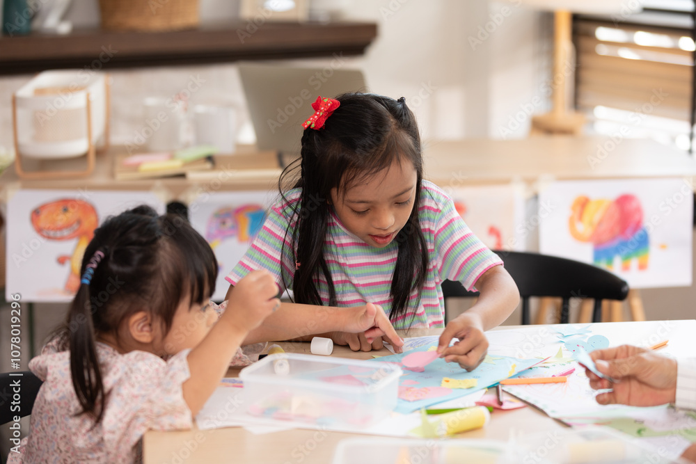 Two young Asian girls with Down syndrome engage in a fun arts and crafts activity, sharing smiles and creativity. They are focused on crafting with colorful materials