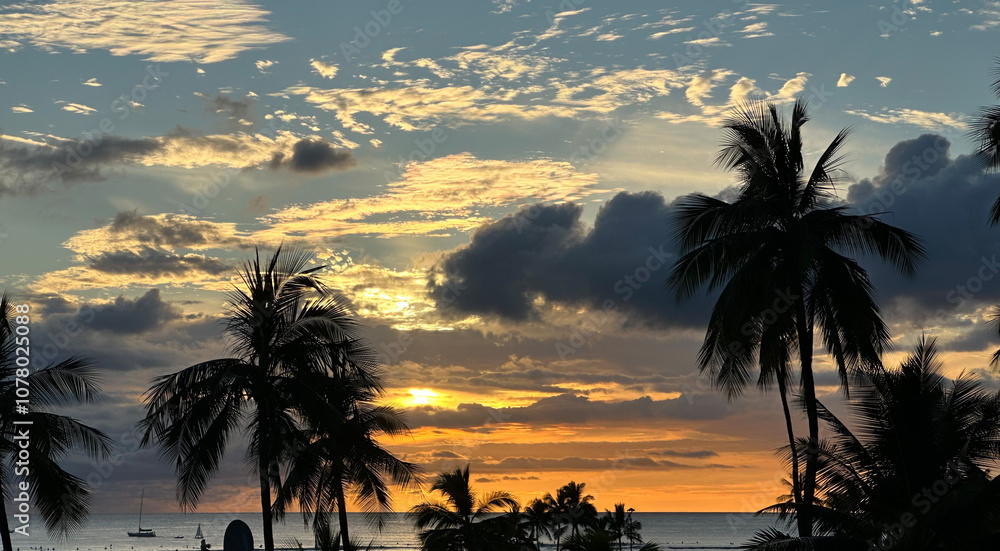 Obraz premium A typical sunset in Oahu Honolulu, which is always stunning! Yellows, oranges, navy blues, clouds, ocean and silhouetted palm trees during golden hour. 
