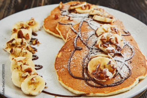 Delicious pancakes topped with sliced bananas, chopped nuts, and chocolate drizzle, creating a delightful and visually appealing breakfast dish photo