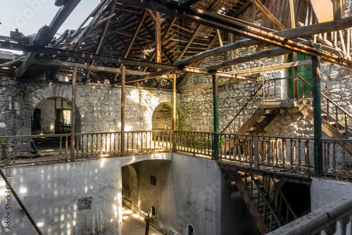 Interior of an old abandoned winery. Stone walls, wooden railings and stairs, a destroyed roof