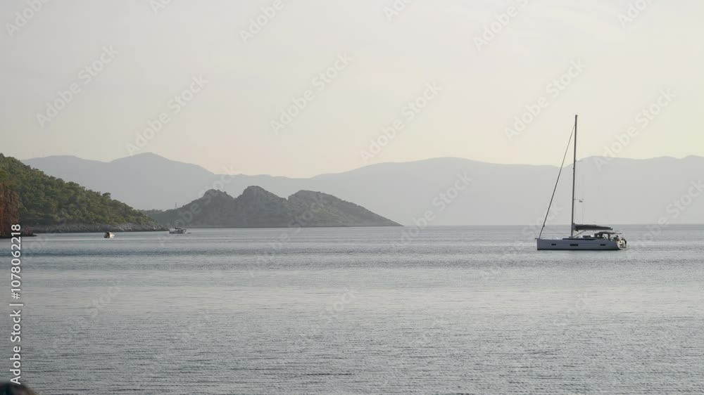 Calm view over ocean with sailing yacht and mountain silhouettes Calm view over ocean with sailing yacht and mountain silhouettes