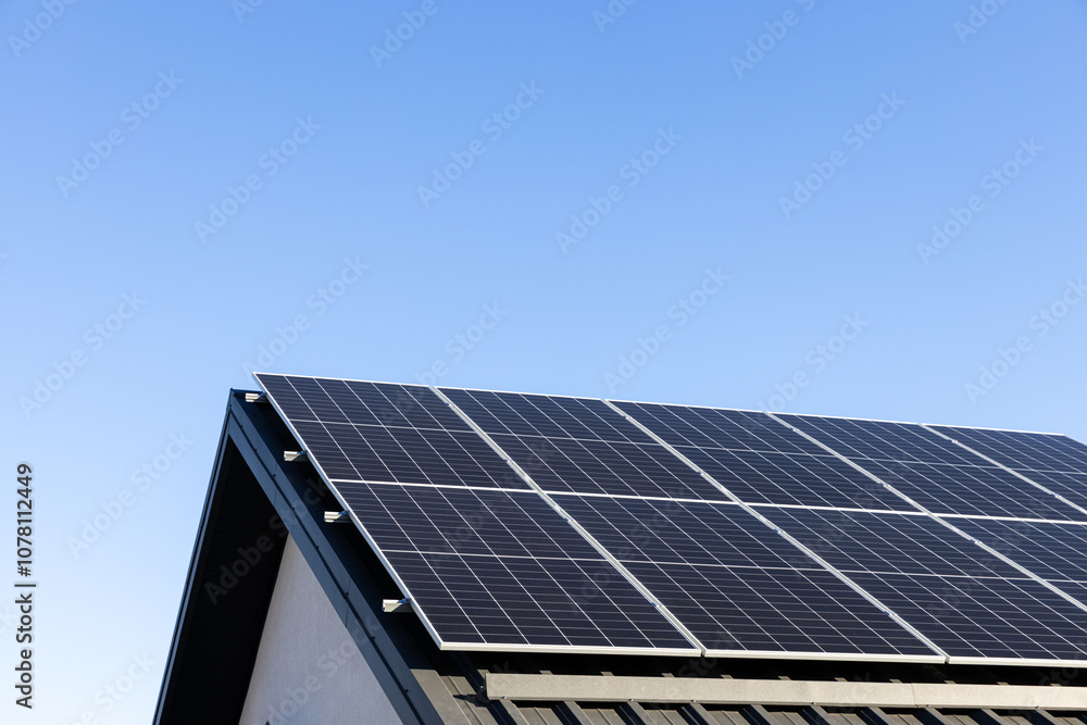 Fototapeta premium Modern house with solar panels stand-alone photovoltaic plant system on household metal sheet rooftop. Clear blue sky background. Clean alternative energy concept. Professional installation, go green