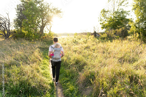 Father hiking in a field with a little girl in a carrier on his back photo