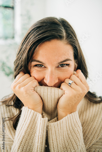 Woman playfully hides face in cozy sweater, showing eyes and smile photo