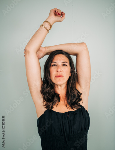 Woman in black dress with arms raised, looking confidently ahead photo