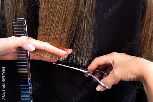 hands of a hairdresser cutting the chopped ends of a long blonde female hair with scissors and a comb.