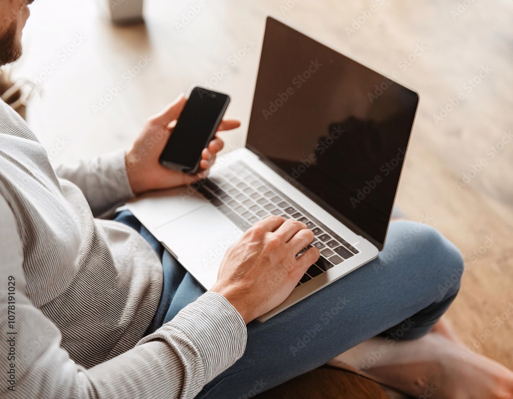 a man who is using a laptop while holding a smartphone. a man who is using a laptop while holding a smartphone.