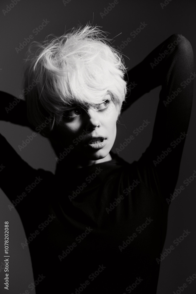 Black and white portrait of a young woman with short blonde hair, striking a thoughtful pose against a dark background. Emotional and artistic expression concept. Black and white portrait of a young woman with short blonde hair, striking a thoughtful pose against a dark background. Emotional and artistic expression concept.