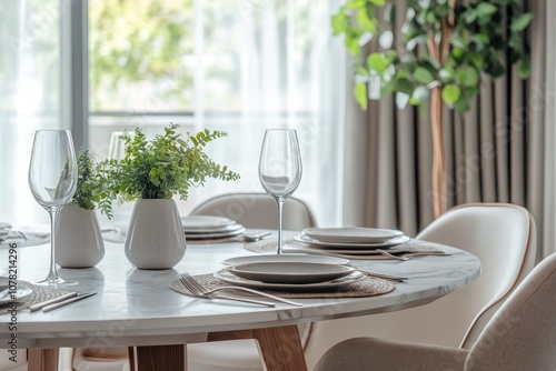 Close-up of a modern dining table setting with white plates, wine glasses, and a potted plant.