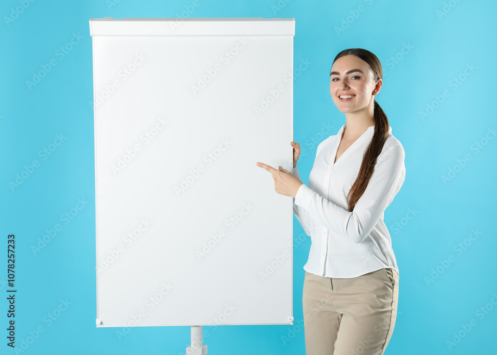 Happy woman near flip chart on light blue background. Mockup for design Happy woman near flip chart on light blue background. Mockup for design