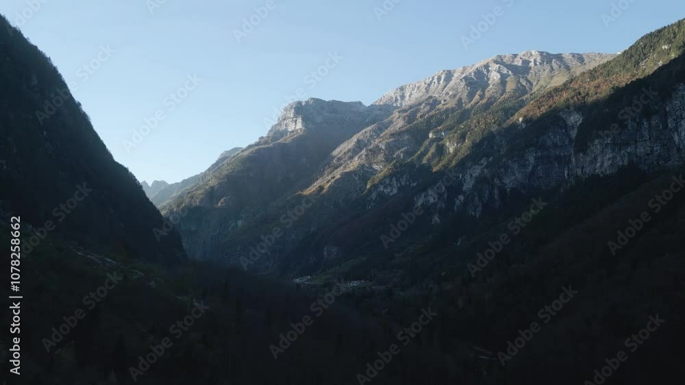 Drone view over a mountain valley in Friuli, Italy: expansive green meadows, winding streams, and rugged peaks surround the valley, with clear skies and a tranquil, picturesque natural landscape Drone view over a mountain valley in Friuli, Italy: expansive green meadows, winding streams, and rugged peaks surround the valley, with clear skies and a tranquil, picturesque natural landscape