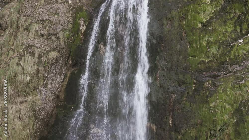 Drone view over Goriuda Waterfall, Italy: water cascades dramatically down rocky cliffs into a crystal-clear pool below, surrounded by lush forest, creating a serene and picturesque natural scene Drone view over Goriuda Waterfall, Italy: water cascades dramatically down rocky cliffs into a crystal-clear pool below, surrounded by lush forest, creating a serene and picturesque natural scene