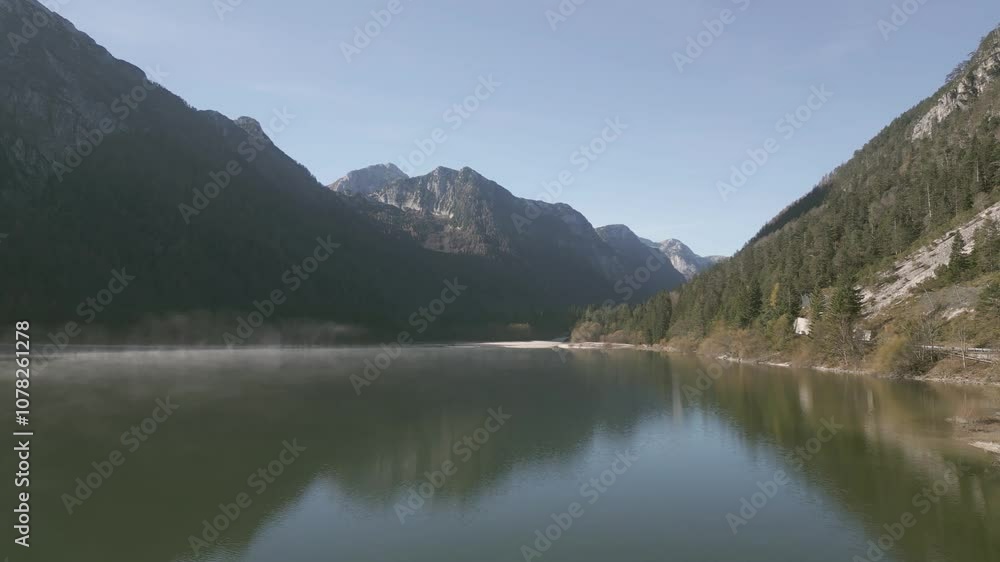 Drone view over Predil Lake, Slovenia: turquoise waters reflect the surrounding mountains, with lush green forests lining the shore. The serene lake is nestled in a valley Drone view over Predil Lake, Slovenia: turquoise waters reflect the surrounding mountains, with lush green forests lining the shore. The serene lake is nestled in a valley