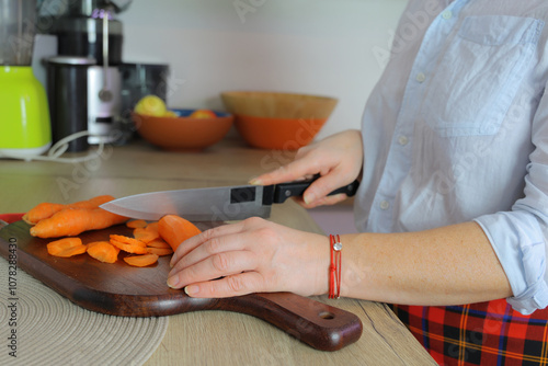 Female with an unrecognized face cut the carrot into small pieces with a kitchen knife
