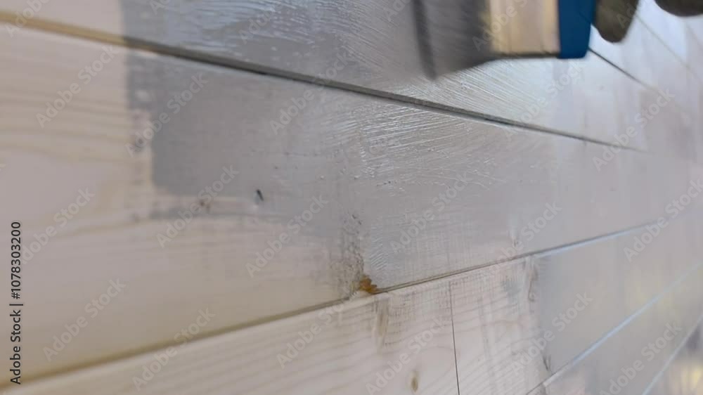 A brush applies gray paint to the wooden house walls, leaving a smooth and uniform coating. The process of protecting and painting the facade. A brush applies gray paint to the wooden house walls, leaving a smooth and uniform coating. The process of protecting and painting the facade.
