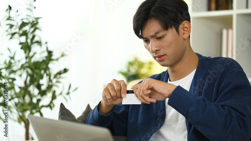 Young asian man destroying his credit card in frustration. Financial management and debt reduction concept photo