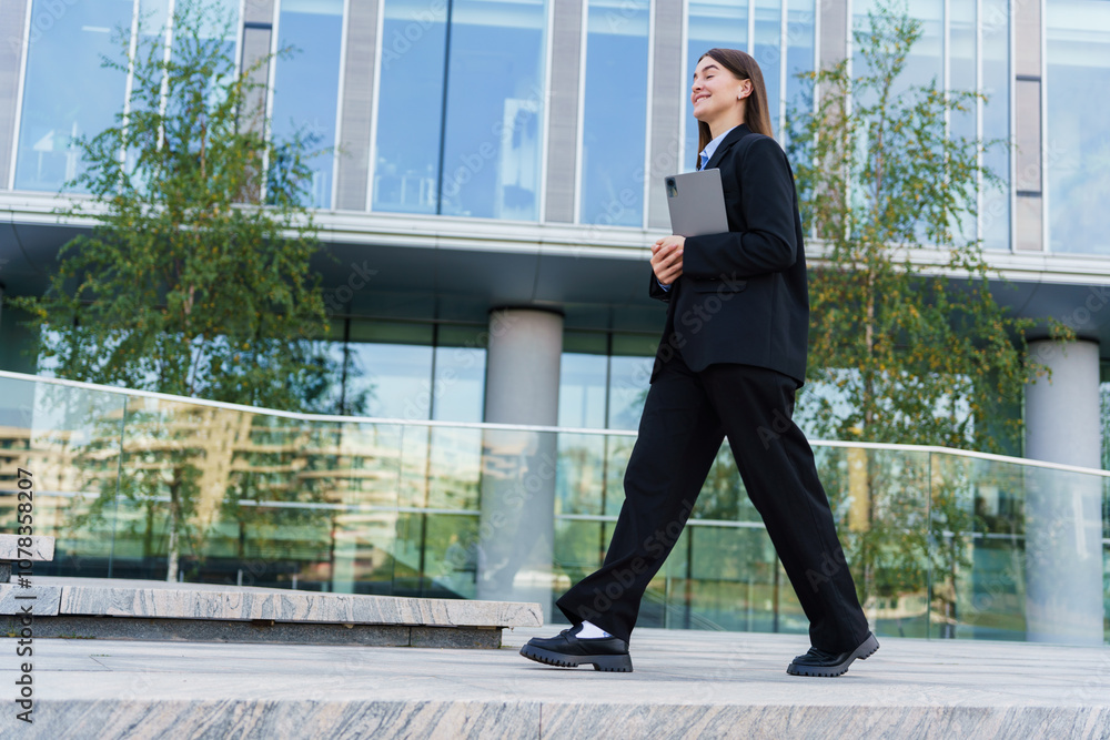 A Businesswoman Walks Confidently Outside a Modern Office Building During Daytime in the City A Businesswoman Walks Confidently Outside a Modern Office Building During Daytime in the City