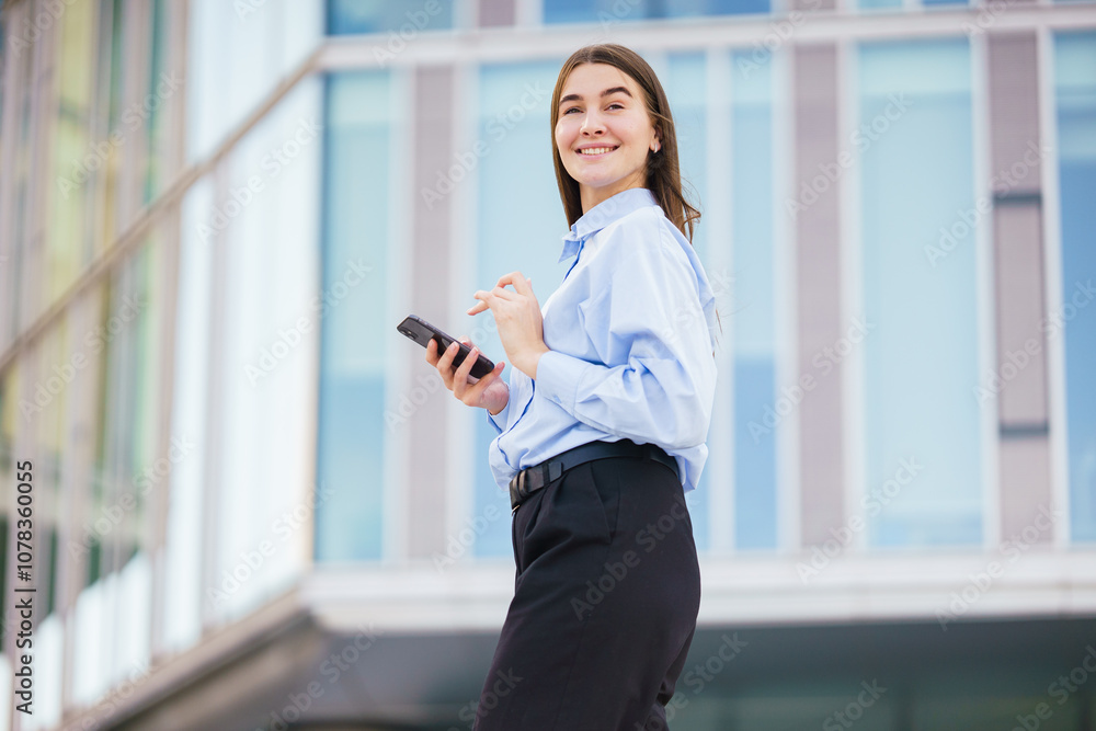 Young Woman Smiles While Using a Smartphone Outside a Modern Glass Building During the Day Young Woman Smiles While Using a Smartphone Outside a Modern Glass Building During the Day