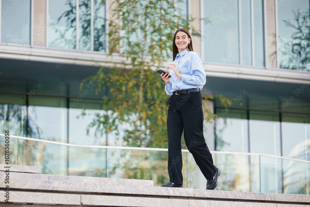 A Woman in Business Attire Walks Confidently Down Steps With a Device in Hand, Enjoying a Sunny Day Outdoors A Woman in Business Attire Walks Confidently Down Steps With a Device in Hand, Enjoying a Sunny Day Outdoors