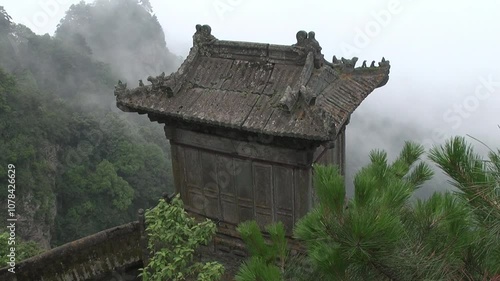 Ancient Taoist temple in the Wudang Mountains, China, partially shrouded in mist. The ornate rooftop and dense surrounding forest create a mystical, spiritual atmosphere.