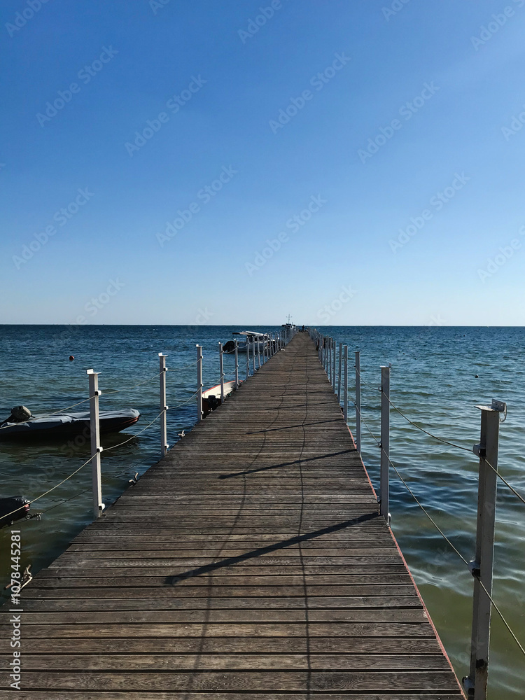 Long wooden pier extending into calm blue ocean under clear sky