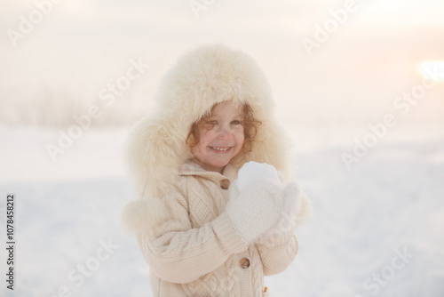 Winter lifestyle portrait of cheerful little girl in knitted sweater throwing snow in the air. Child is smiling and having fun in the snow park. Freedom and happiness concept.