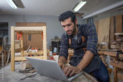 young carpenter caucasian man with laptop make drawing on wood to design at workspace. craftsman profession in wood factory photo