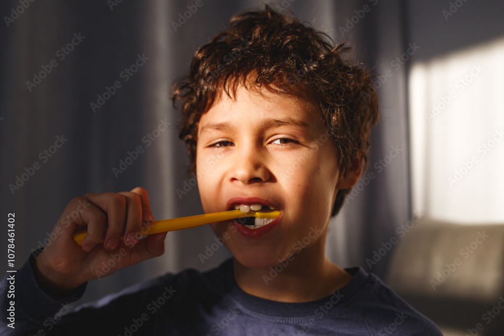 Happy curly boy brushing his teeth by yellow brush with toothpaste at sunny morning in living room Happy curly boy brushing his teeth by yellow brush with toothpaste at sunny morning in living room