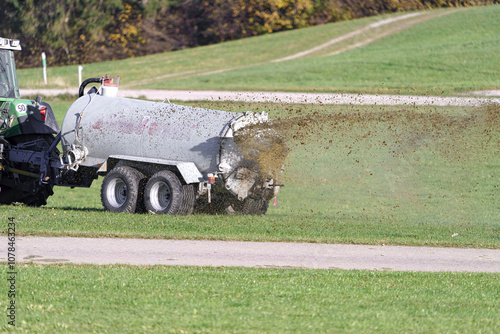 A tractor in an agricultural field spreads manure from a tanker and fertilizes grassy vegetation for cattle feed. Fertilizer and vegetation in agriculture. photo